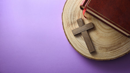 Religious background with tools for prayer with a Bible on wooden base with Christian cross on lilac table. Top view.の写真素材