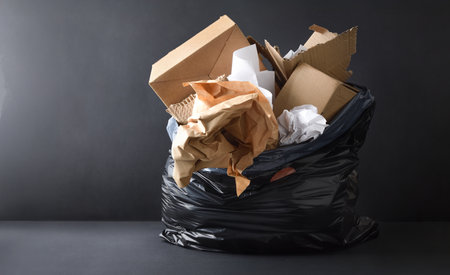 Background with detail of black plastic garbage bag full of paper and cardboard isolated on dark background and base. Front view.の写真素材