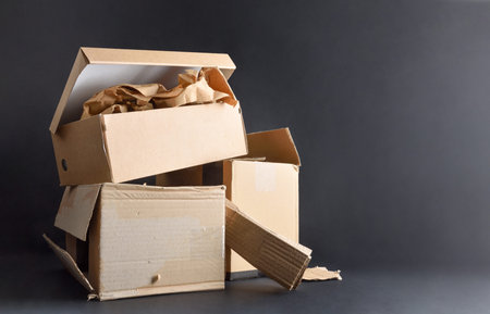 Paper and cardboard pollution and recycling concept with pile of cardboard boxes on a black base isolated on a black background. Front view.の写真素材