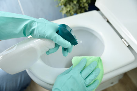 Detail of hand of man with green rubber gloves and disinfectant spray bottle scrubbing toilet bowl. Elevated view.の写真素材
