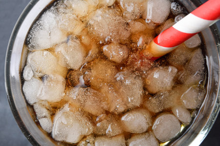 Detail of the mouth of a transparent glass with a refreshing drink with ice and a white and red...