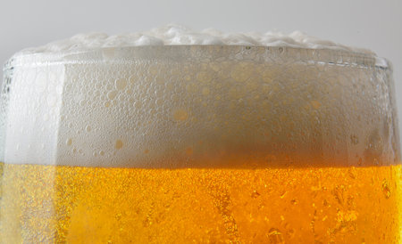 Detail of the mouth of a glass of beer filled with foam, isolated on a light background. Front view.の写真素材
