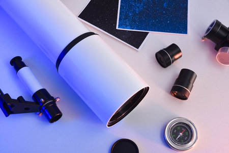 Telescope different parts spread out on a white table with tripod and photos of the universe illuminated with blue light. Top view.の写真素材