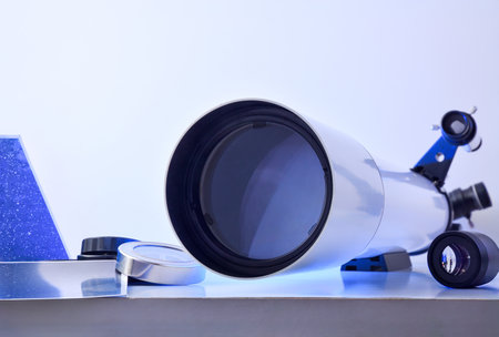 View of a telescope lens on a white table with various material for astronomical study and books and photos on a white background. Front view.の写真素材