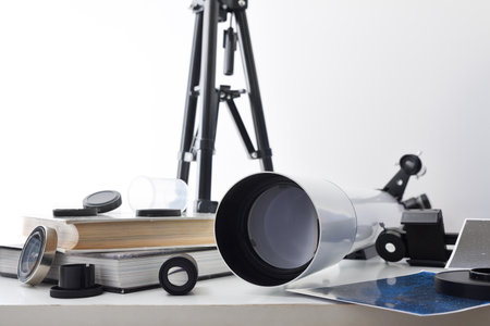 View of a telescope lens on a white table with various material for astronomical study and books and photos on a white background. Front view.の写真素材