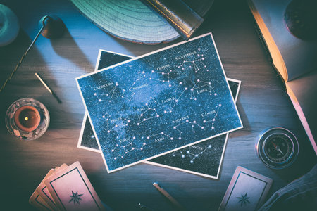 Astrological background of study and forecast with maps with constellations in the center of a wooden table with vintage objects and tools around with magical atmosphere. Top view.の写真素材