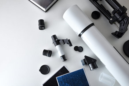 Parts and spares of a telescope on a white table with photos and a book. Top view.