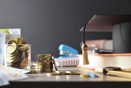 High cost of education concept with money and educational supplies on wooden table and dark isolated background. Front view.の写真素材
