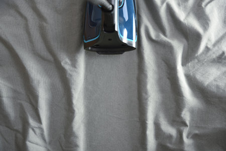 Detail of an iron passing over a wrinkled gray fabric, leaving a freshly ironed line in the center. Top view.の写真素材