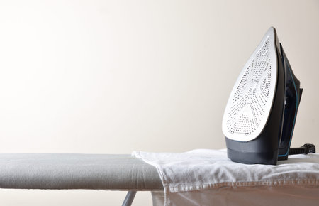 Home ironing concept with iron resting on gray ironing board with white shirt and light isolated...