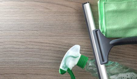 Window cleaner spatula, spray product and microfibre cloth isolated on wooden table. Top view.