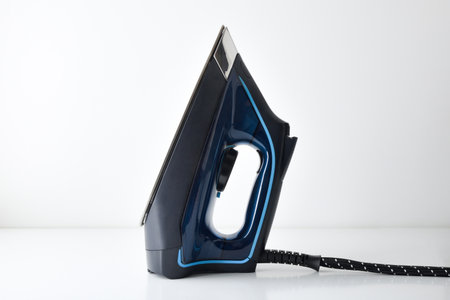 Side view of blue steam iron reflected and supported vertically on white table with white isolated background. Front composition.の写真素材