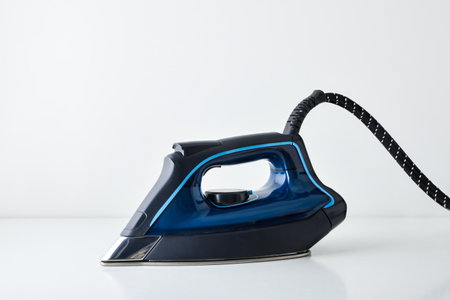 Blue steam iron resting on white table with reflection and white isolated background side view.の写真素材