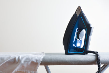 Home ironing concept with steam iron on ironing board with white shirt and white isolated background. Front view.の写真素材