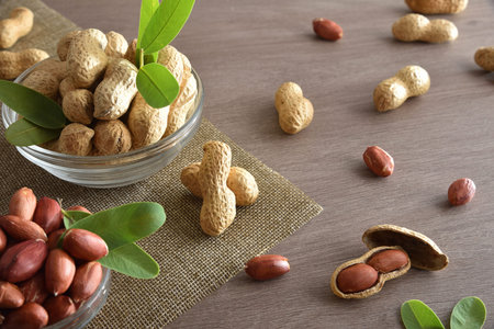 Peeled and unpeeled peanuts in glass bowls on a wooden kitchen bench. Elevated view.