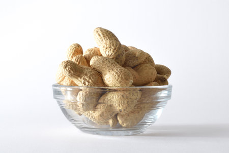 Detail of a glass bowl with a pile of peanuts, isolated on white background. Front view.の写真素材