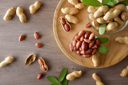 Peeled and unpeeled peanuts in glass bowls on a wooden plate on kitchen bench. Top view.