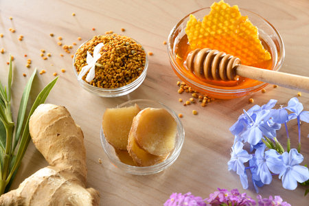Natural painkillers and healing products in glass bowls, such as ginger root, honey, and pollen. Wooden table setting with leaves and flowers. Elevated view.の写真素材