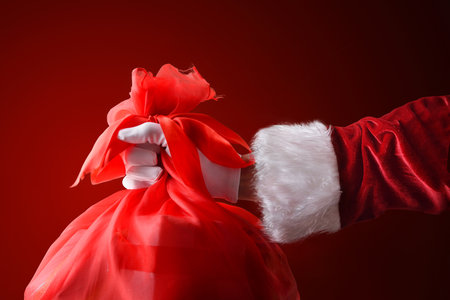 Santa Claus's hand in a suit and gloves holding a red sack with gifts to hand out at Christmas.の写真素材