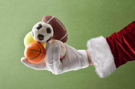 Hand in suit and gloves holding small balls of various sports on green isolated background. Competition concept of various ball sports.の写真素材