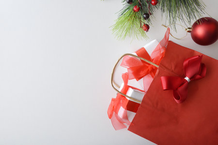 Christmas shopping concept with red paper shopping bag with ribbon full of gifts isolated on white table with Christmas decoration. Top view.の写真素材
