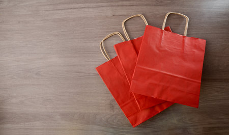 Pack of three empty red paper shopping bags with brown twisted paper handles folded on a wooden table. Top view.の写真素材