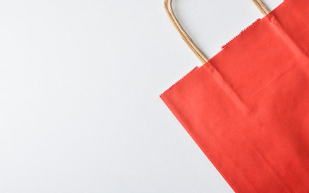 Detail of an empty, folded red paper shopping bag with brown braided paper handles on a white background. Top view.の写真素材