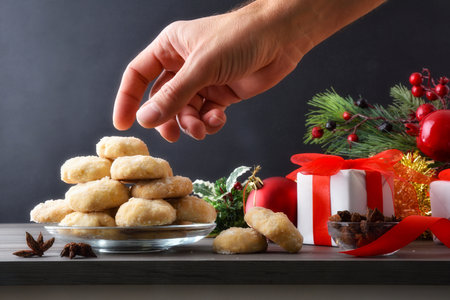 Tasting anise cookies from a glass plate on a table with Christmas decorations and dark isolated background. Front view.の写真素材