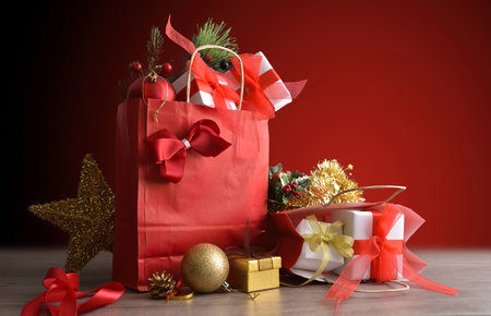 Concept of giving gifts at Christmas with red gift bags full of gift packages and Christmas decorations on a wooden table and red gradient background.の写真素材