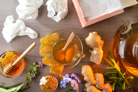 Natural infusion made from ginger root and honey in a glass cup as a good home remedy for colds and congestion on a wooden table with used tissues and a box of tissues. Top view.の写真素材