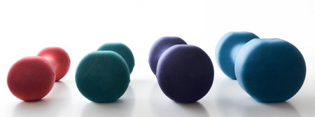 Collection of neoprene dumbbells of different weights and colors in a row reflected on a white table and isolated white background.の写真素材