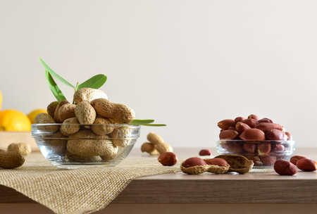 Peeled and unpeeled peanuts in glass bowls on a wooden kitchen bench and white isolated background....