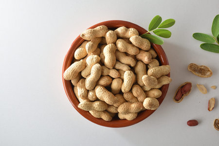 Heap of peanuts with skin in a brown clay bowl with leaves placed in the center isolated on a white...