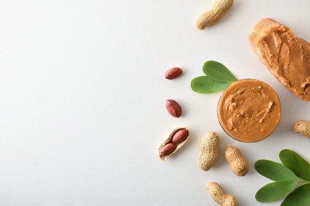 Bowl full of peanut butter and slice of bread on white table with fruits and leaves. Top view.の写真素材