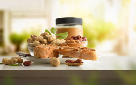 Slices of bread with peanut butter on a white plate with bowls of peanuts and a jar full of peanut...