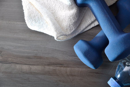Concept of sport, training and wellness with two blue neoprene dumbbells on a wooden floor with a water bottle and white towel around. top viewの写真素材