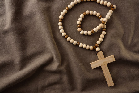 Close-up of a wooden rosary with cross placed on brown fabric. Spiritual and religious concept...