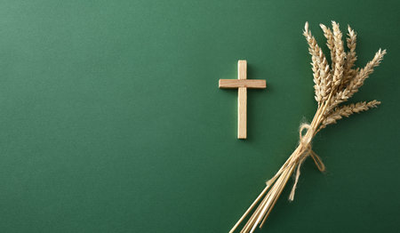 Wooden cross beside a bundle of wheat on a green background. Symbolic Christian composition...
