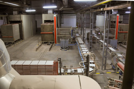 Wide view of a ceramic tile factory floor showing automated conveyors, stacked tiles, and large kiln units used in industrial tile manufacturing.の写真素材