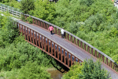 Old man and woman walking on the old wooden bridge over the riverの写真素材