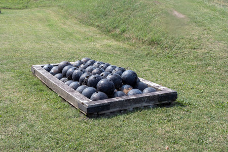 Cannonballs in a wooden box on a green grass field.