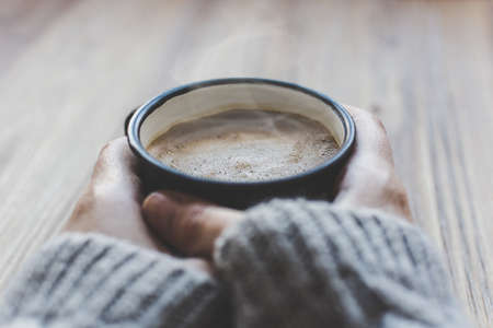 view of the female hands warming herself with the hot coffee on the wooden backgroundの写真素材