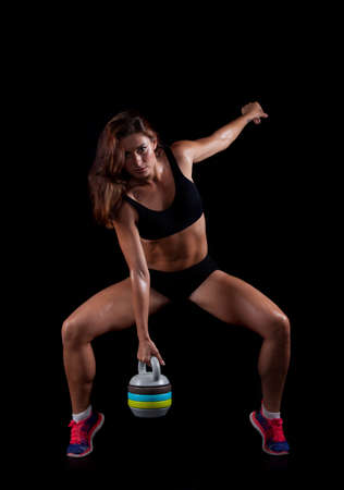 Young sporty girl with the sweat on the skin does exercise standing with weights on a black background.の写真素材