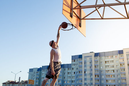 One guy play basketball at district sports ground against a backdrop of high-rise residential...
