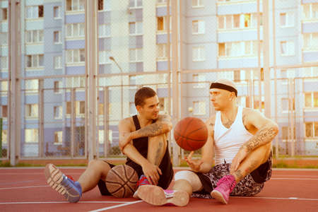 Two guys are sitting on the basketball court with balls and communicate. Spin the ball on his finger.の写真素材