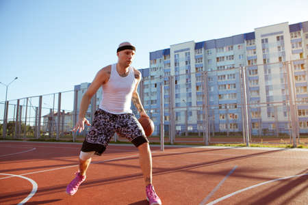 Guy plays basketball on a red Court in sunny weather.の写真素材