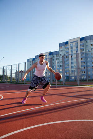 Guy plays basketball on a red Court in sunny weather.の写真素材