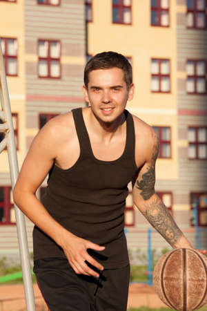 Guy plays basketball on a red Court in sunny weather.の写真素材
