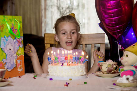 Little girl's birthday sitting at a table in front of the cake and looks at the camera.の写真素材