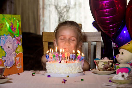 Little girl's birthday sitting at a table in front of the cake and looks at the camera.の写真素材